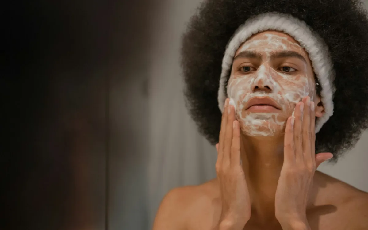 Primer plano de un hombre joven en un baño luminoso, aplicando o ajustando parches blancos para los ojos sobre su piel, como parte de una rutina de skincare masculino y cuidado personal.