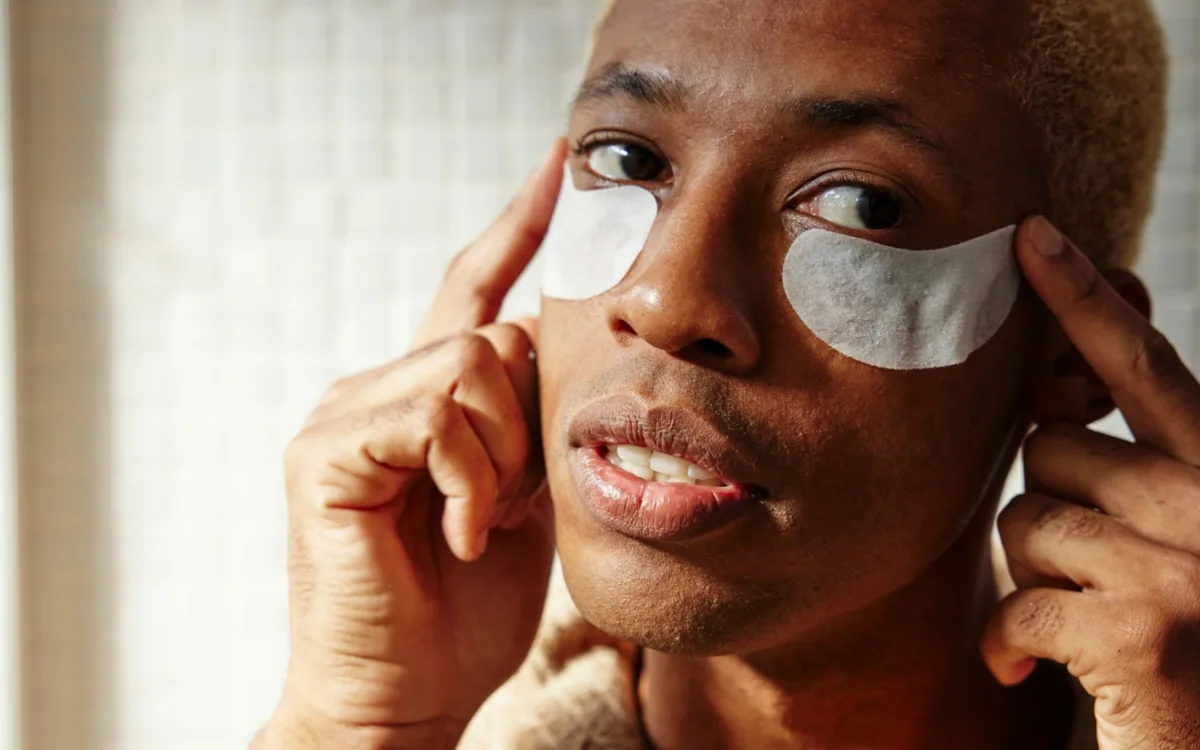 Primer plano de un hombre relajado con parches de hidrogel blancos, destacando el cuidado facial para caballeros y el bienestar personal.